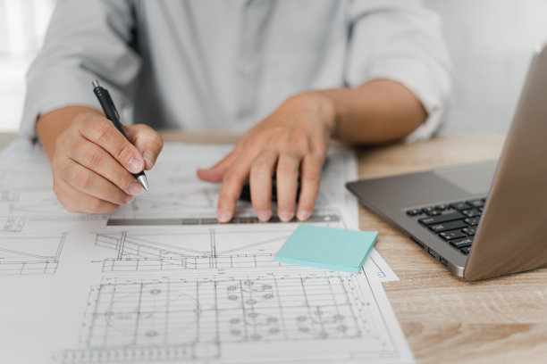 工程工作理念:在办公室的木桌上用铅笔和钢尺标注CAD图和计算文档中的计算器和笔记本电脑图片下载