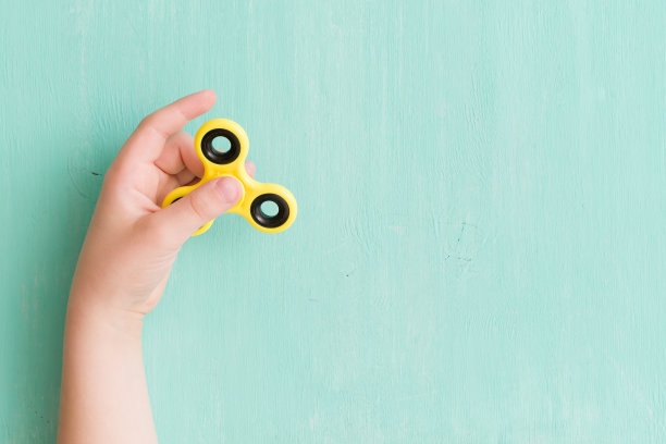 孩子的手在蓝绿色的背景上旋转指尖陀螺。前视图。玩一个手摇陀螺玩具图片下载