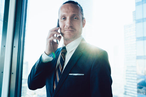 西装革履的商人正对着手机轻声微笑图片下载