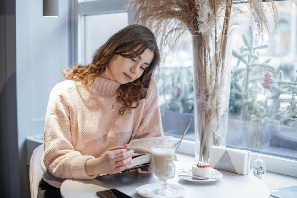 美丽女人的肖像，一边在咖啡馆里看书，一边放松。图片下载