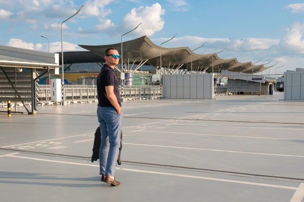 一个年轻人带着行李走在机场城的街道上。商务旅行，都市生活图片下载
