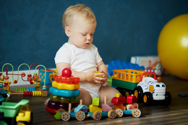 可爱的小男孩坐在家里的地板上玩玩具。儿童的早期发展。快乐的童年。儿童产品广告图片下载