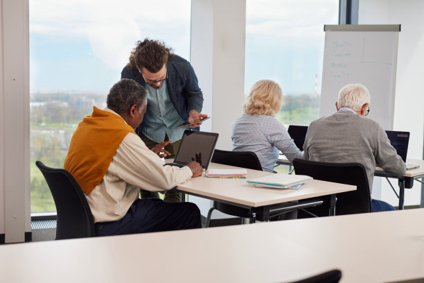 当其他学生使用笔记本电脑时，一位老师正在向学生展示如何创建优秀的网页设计。图片下载