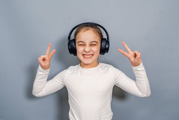 戴着耳机的精力充沛的小女孩。白色t恤，闭着眼睛，手指摆出胜利的手势。图片下载