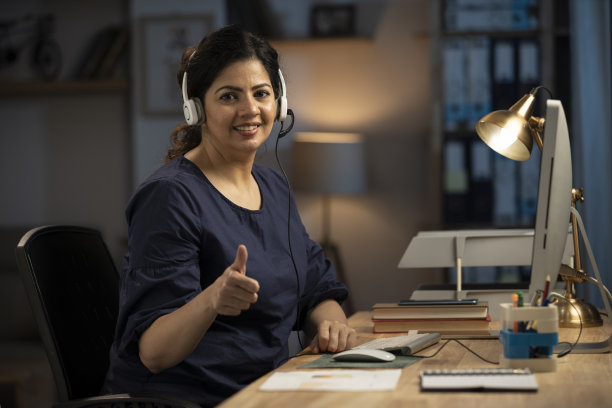 年轻女性使用耳机和台式电脑在家庭办公室的股票照片图片下载