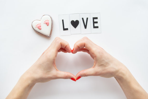 女人的手在一个心形孤立在一个白色的背景，侧面的碑文爱和一个小的心与婴儿的脚的足迹。图片下载