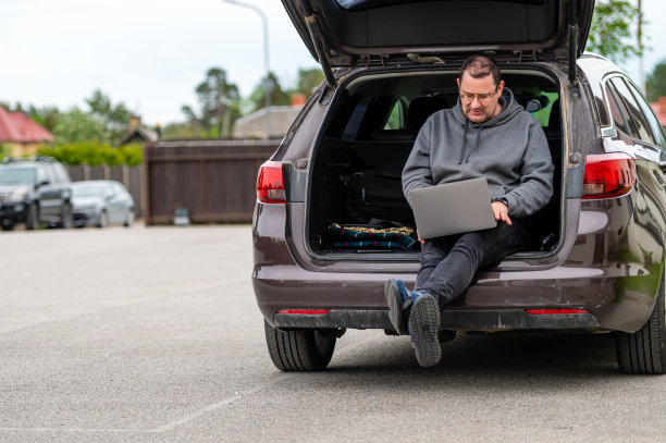 一个男人坐在敞开的后备箱里用笔记本电脑工作，移动技术，远程工作图片下载