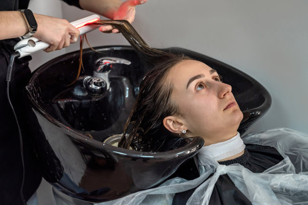 女孩坐在沙龙里，她的化妆师正在给她洗头和头发，准备上色。图片下载