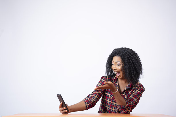 美丽的黑人女性坐在那里用手机，看起来既惊讶又兴奋图片下载