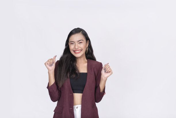 一位漂亮的亚洲女士对即将到来的拍卖感到头晕目眩，激动地举起双臂。穿着紫褐色运动上衣和黑色筒形上衣。孤立在白色背景。图片下载