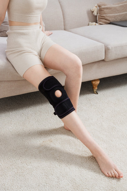 女人腿上的膝盖支撑支架。女孩戴着矫形器在屋子里。骨科解剖支架，用于膝关节固定、损伤和疼痛。膝关节绷带套筒。弹性运动图片下载