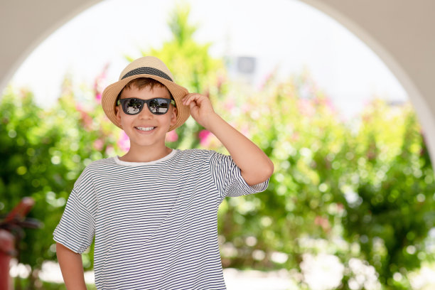 在阳光明媚的日子里，英俊微笑的夏天孩子的肖像。快乐微笑的学生在条纹t恤和太阳镜摆出户外看着相机。图片下载