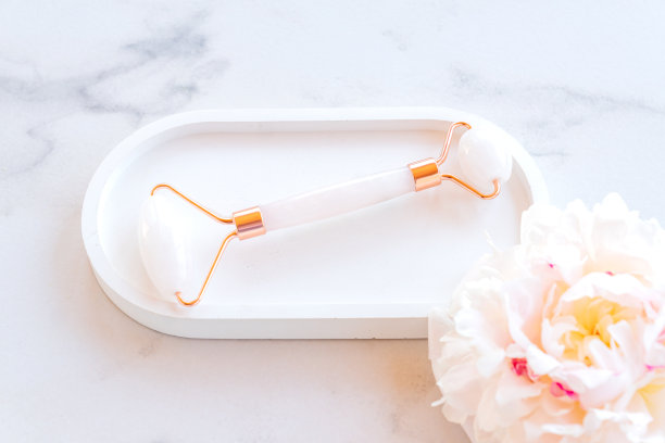 粉色瓜沙按摩工具在混凝土托盘大理石背景与牡丹。玫瑰石英玉辊。家庭皮肤护理、抗衰老、提升疗法。前视图。副本的空间。生活方式图片下载