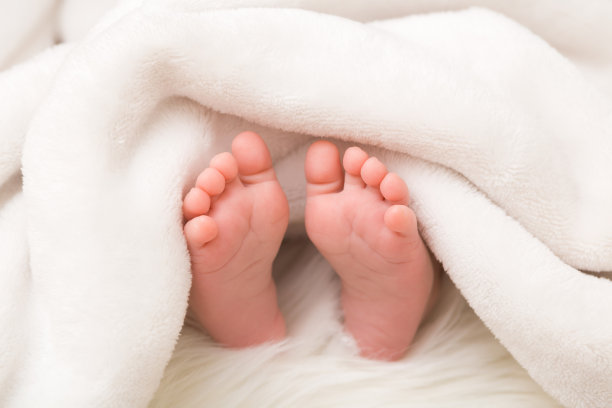 新生儿赤脚躺在床上。脚伸出白色柔软的毯子。宝宝睡觉。特写镜头。图片下载