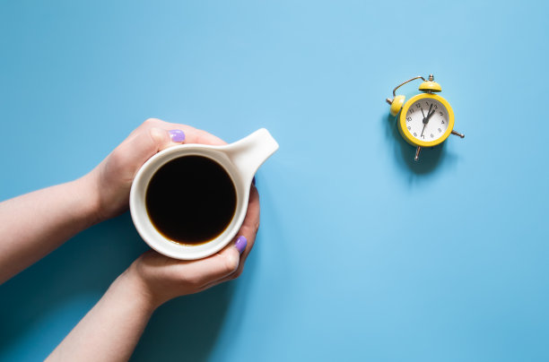 一杯女性手中的咖啡和一个蓝色背景的闹钟。图片下载