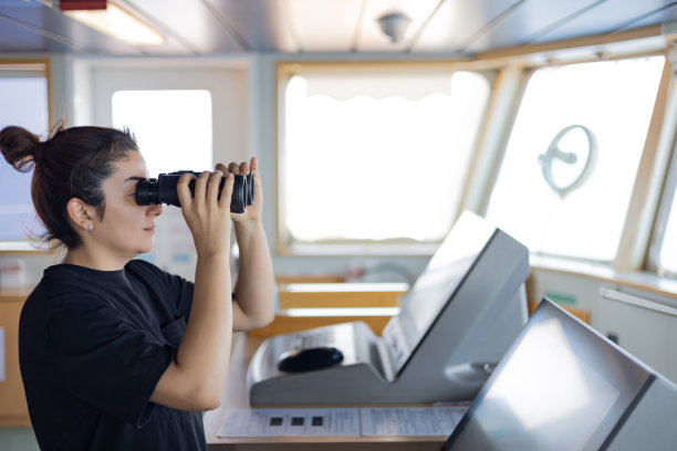 年轻美丽的女船长在船的控制中心用望远镜观察周围的环境。图片下载