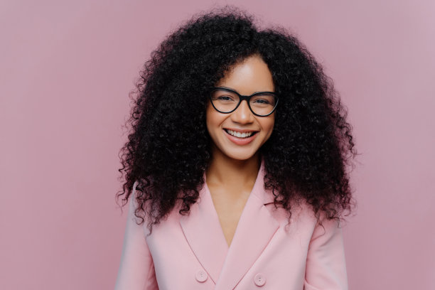 快乐的卷发女人的特写肖像脸上有温柔的微笑，深色健康的皮肤浓密的头发，穿着优雅的衣服，孤立在紫色的背景，享受即将到来的周末，在办公室工作图片下载