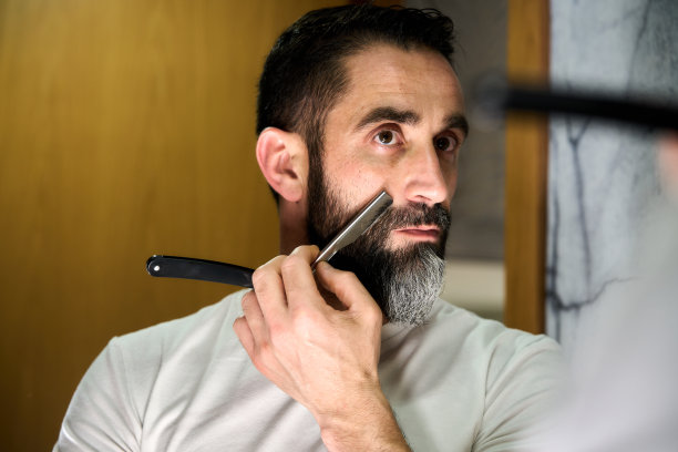 年轻男子在镜子前用传统的刀剃须图片下载