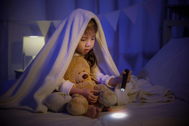 孩子亚洲女孩玩玩具熊与手电筒下的毛毯在床上在黑暗的卧室在晚上睡觉前，舒适的孩子在家里的概念图片下载