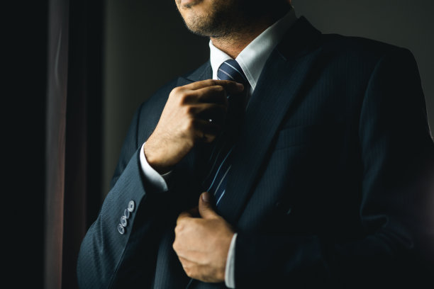 清晨，自信的商人在酒店房间靠窗处系扣子或调整经典的蓝色西装。一个帅哥在婚礼上穿了一套漂亮的西装。图片下载