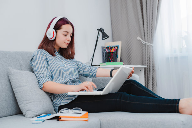 年轻的女孩十几岁的学生坐在地板客厅沙发学生在家学习，用她的笔记本电脑做作业图片下载