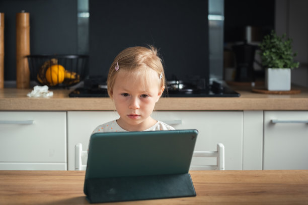 可爱的白人小女孩看卡通平板电脑在时尚的内部图片下载