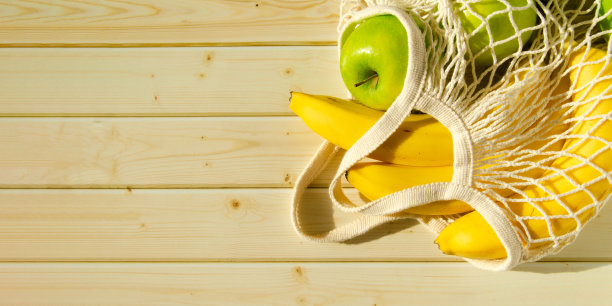 新鲜水果装在网袋里。俯视图，香蕉和苹果在一个绳子袋在木制背景。图片下载