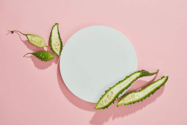 苦瓜在培养皿中的俯视图，绿叶和空白的粉红色背景图片下载