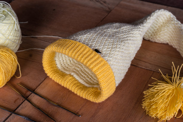 美丽的冬季帽子设计，由哥伦比亚工匠。用钩针技术编织的精灵帽子，放在一块木板上，一边有一卷羊毛和针。图片下载