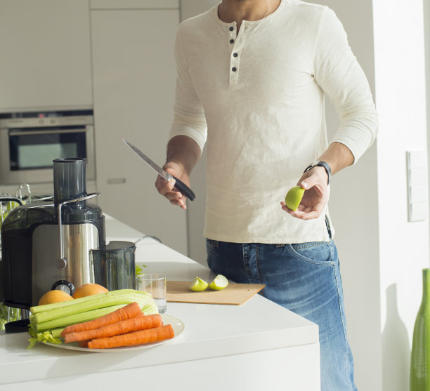 男子准备纯素新鲜果汁。年轻健康的运动男在厨房做饭，在搅拌机里切和搅拌，喝新鲜的蔬菜，新鲜的苹果。素食健康饮食理念图片下载