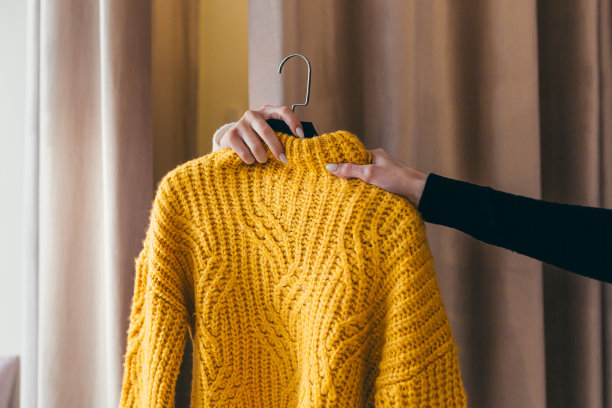 特写照片。销售人员或顾问把挂在衣架上的黄色毛衣递给在窗帘后面试衣间等候的客户的手。在购物中心的一家服装店图片下载