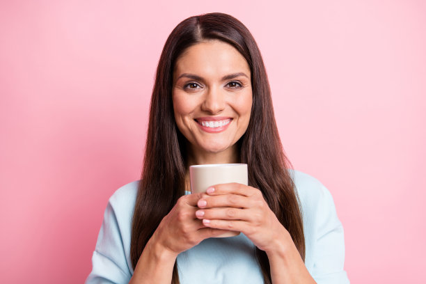 照片肖像微笑漂亮的女人保持杯子与饮料穿着蓝色套头衫孤立的粉彩背景图片下载