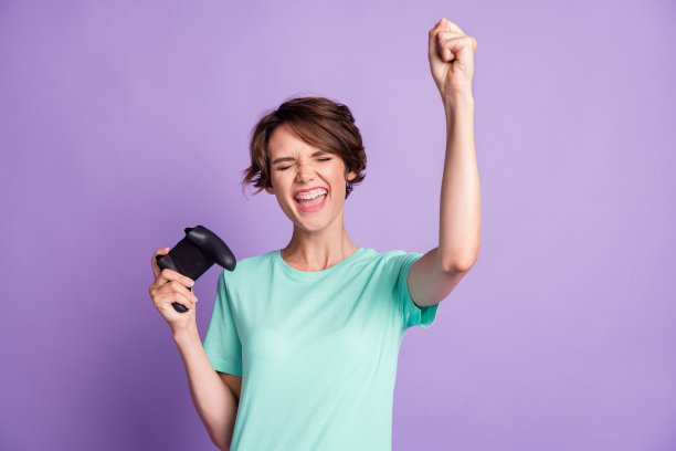 惊讶的年轻女玩家穿着休闲的蓝绿色衣服拿着游戏机孤立的紫色背景的照片图片下载