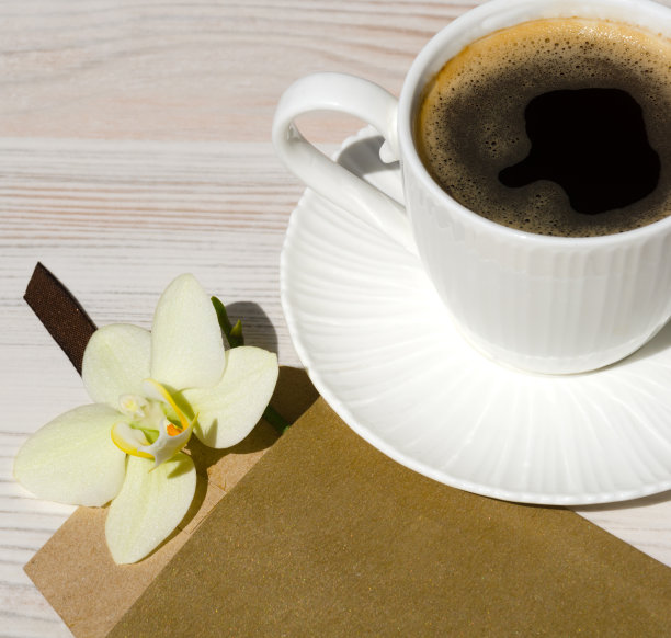 白色的桌子上放着一杯咖啡。兰花的信封。浪漫的早晨。图片下载