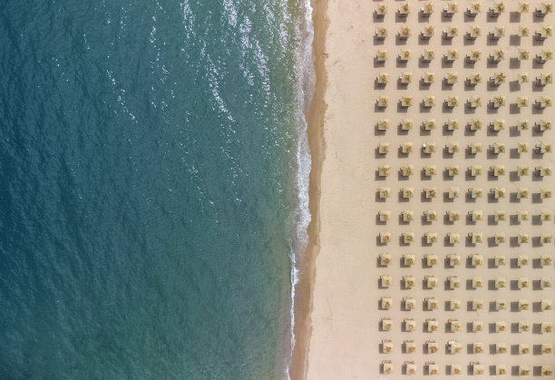 鸟瞰一个令人惊叹的空沙滩，稻草沙滩伞和蓝绿色的清澈的水。图片下载