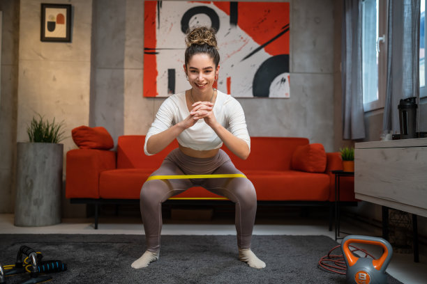 一个女人美丽的女性训练在家里的房间里使用橡胶阻力带腿深蹲和臀部臀大，女运动员做运动独自健康和健身概念复制空间全长图片下载