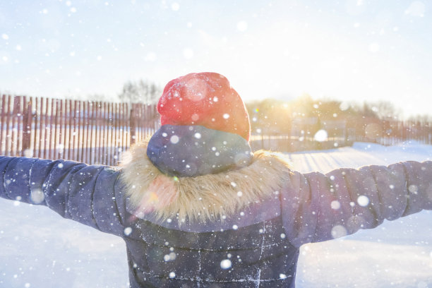 一个孩子在冬天的新鲜空气中伸开双臂，背靠着站着。彩色照片与太阳眩光，选择性聚焦，艺术模糊图片下载