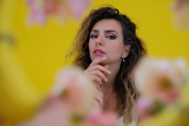 一个美丽女孩的特写肖像在黄色的背景。女子在五彩缤纷的花朵背景下摆姿势。图片下载