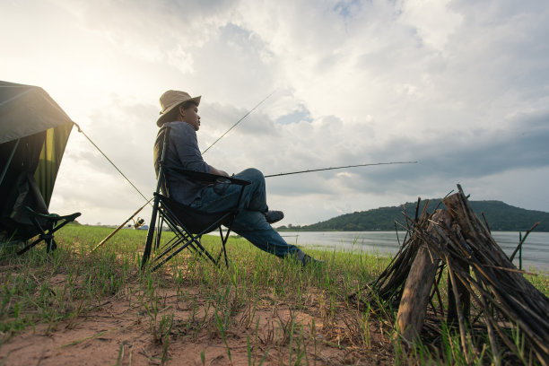 垂钓者坐在椅子上，用篝火在湖边钓鱼。图片下载