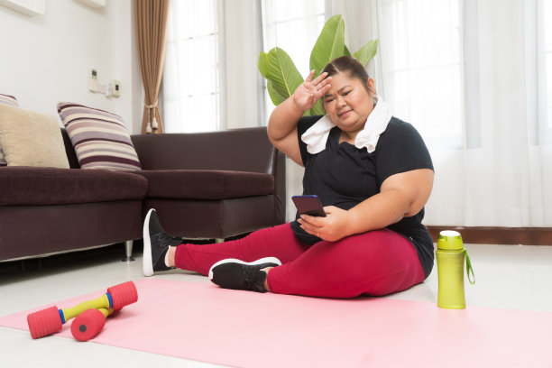 亚洲女性胖累了在家里用智能手机锻炼，运动锻炼、减肥和娱乐的想法概念。图片下载