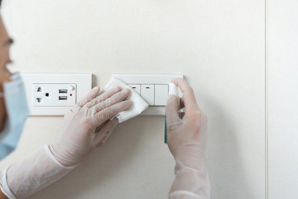 女仆戴上医用口罩，双手戴上橡胶防护手套，用湿巾擦拭和酒精喷雾;擦拭墙上的电灯开关上的灰尘和细菌。清洁;表面消毒的概念。近距离图片下载