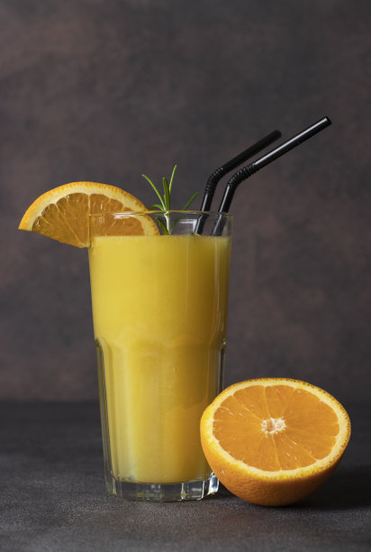 将新鲜橙汁倒入高脚杯中，杯中有一小枝迷迭香，杯底为棕色图片下载