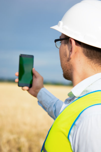 一名工程师正在田里开发他的智能手机，一名农业工程师站在田里，一名工程师手里拿着手机，一名工程师戴着头盔图片下载
