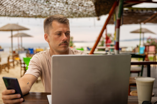 白人男子在海滩咖啡店工作时使用手机图片下载