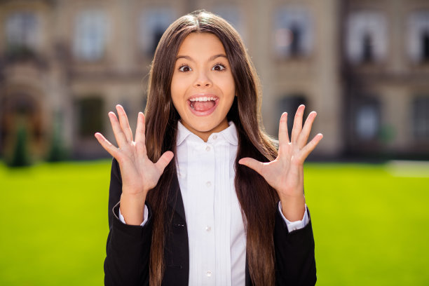 照片中的小小学生女孩兴奋的脸张开嘴举起手掌穿着白色衬衫黑色夹克制服城市外图片下载
