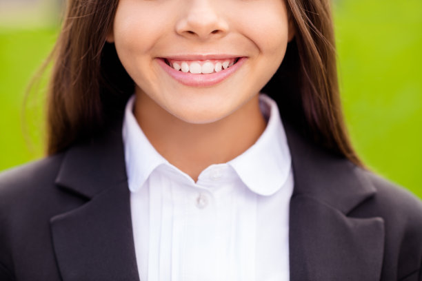 小女孩的照片显示白色的牙齿穿白衬衫黑色夹克制服城市自然户外图片下载