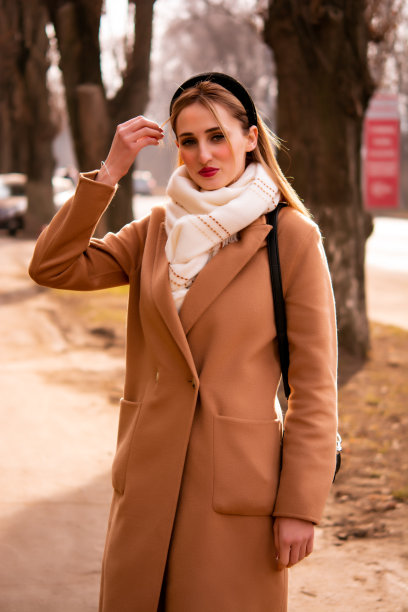 美丽的女孩在条纹风衣和墨镜与小黑色交叉包拿着咖啡走在一起，在舒适的城市街道上深思熟虑图片下载