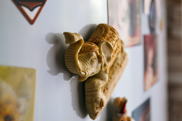 在白色冰箱上挂着一个黄色的印度象雕像，它的鼻子凸起，并在冰箱上投下阴影图片下载