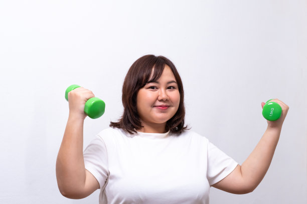 年轻的亚洲胖女人持有哑铃锻炼和重量训练。在减肥过程中，用积极的情绪与饮食抗争。人像拍摄在白色背景。图片下载