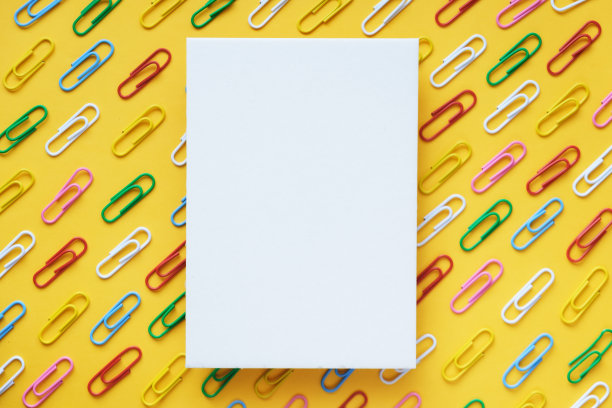 白色空白纸卡的背景多色回形针的黄色背景。图片下载